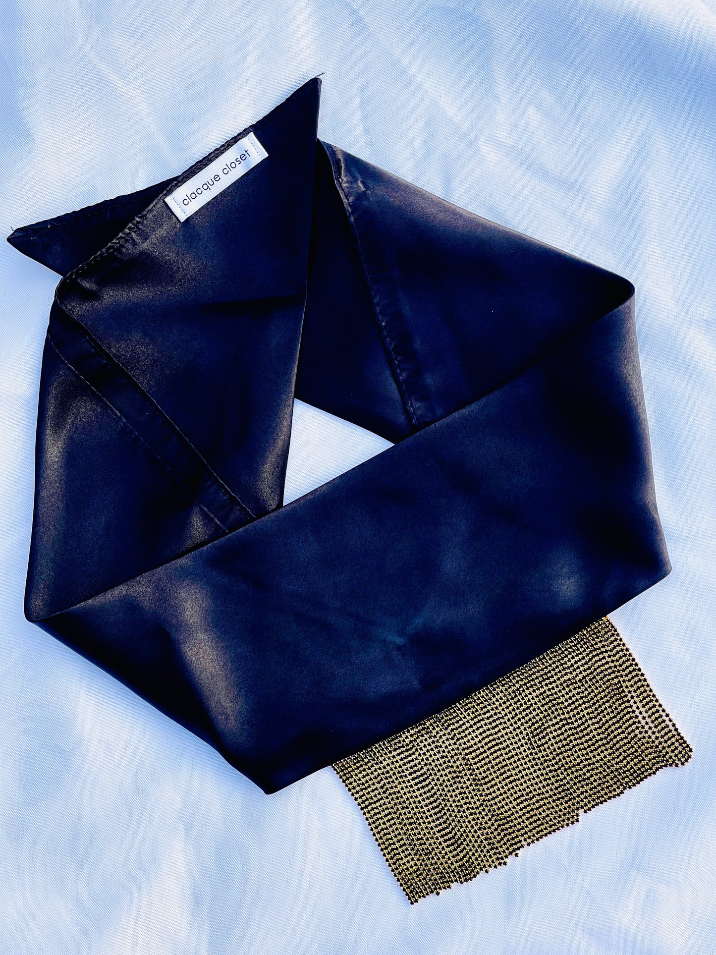 Minerva black satin bandana bang with gold fringe laid flat.