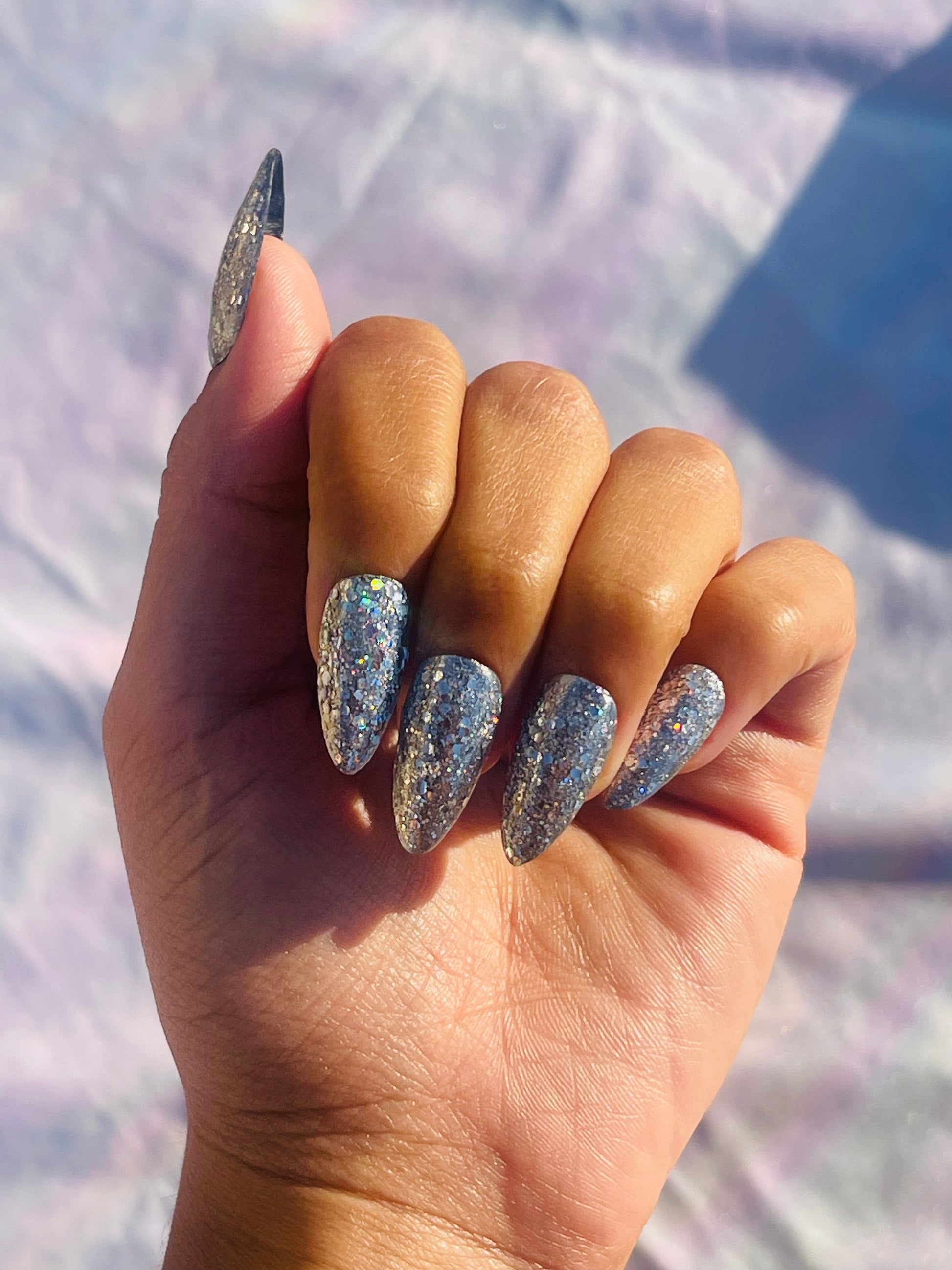 A set of medium-length, almond-shaped nails covered in silver glitter, showcasing a sparkling and elegant appearance.