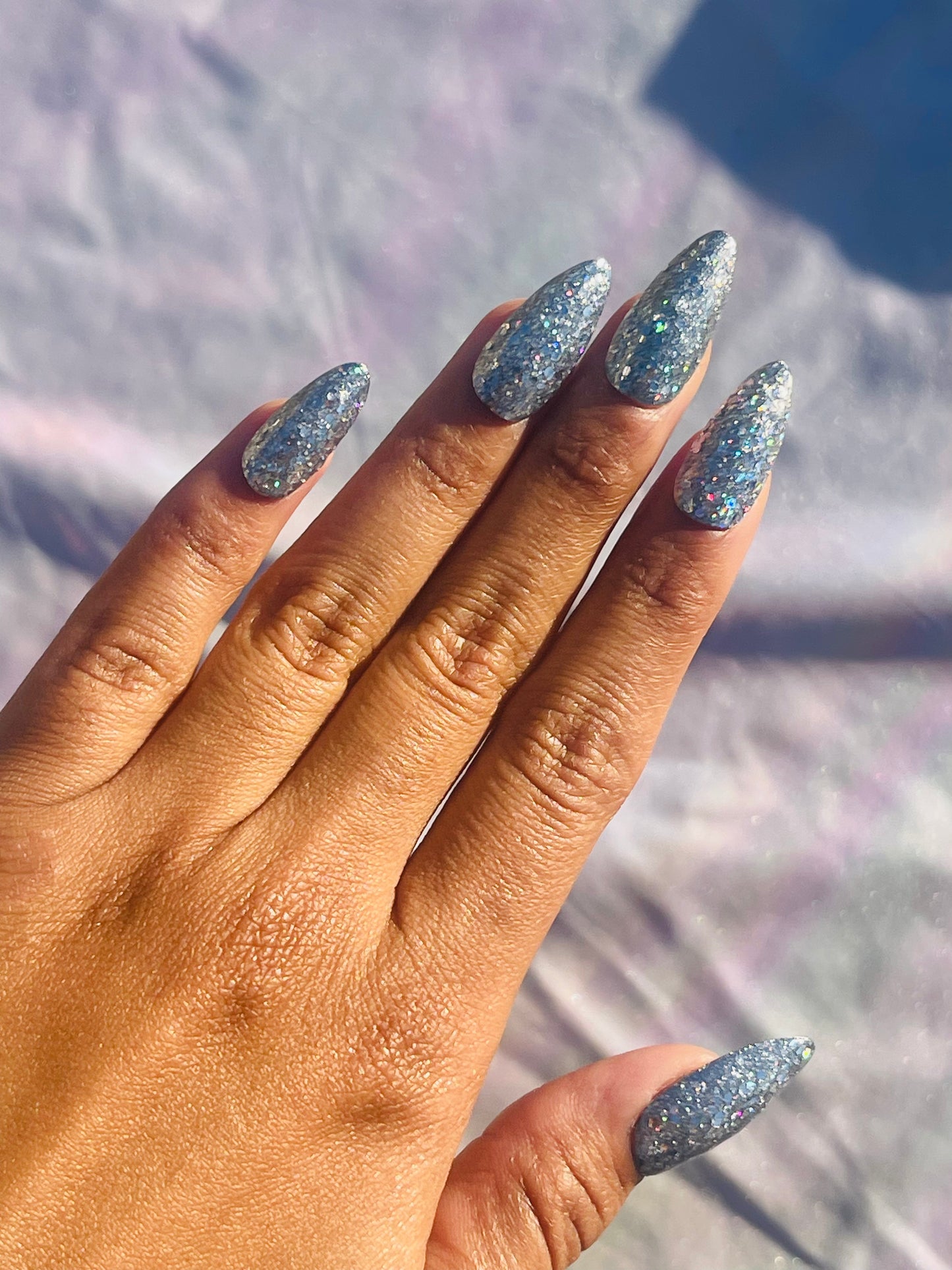 A set of medium-length, almond-shaped nails covered in silver glitter, showcasing a sparkling and elegant appearance.