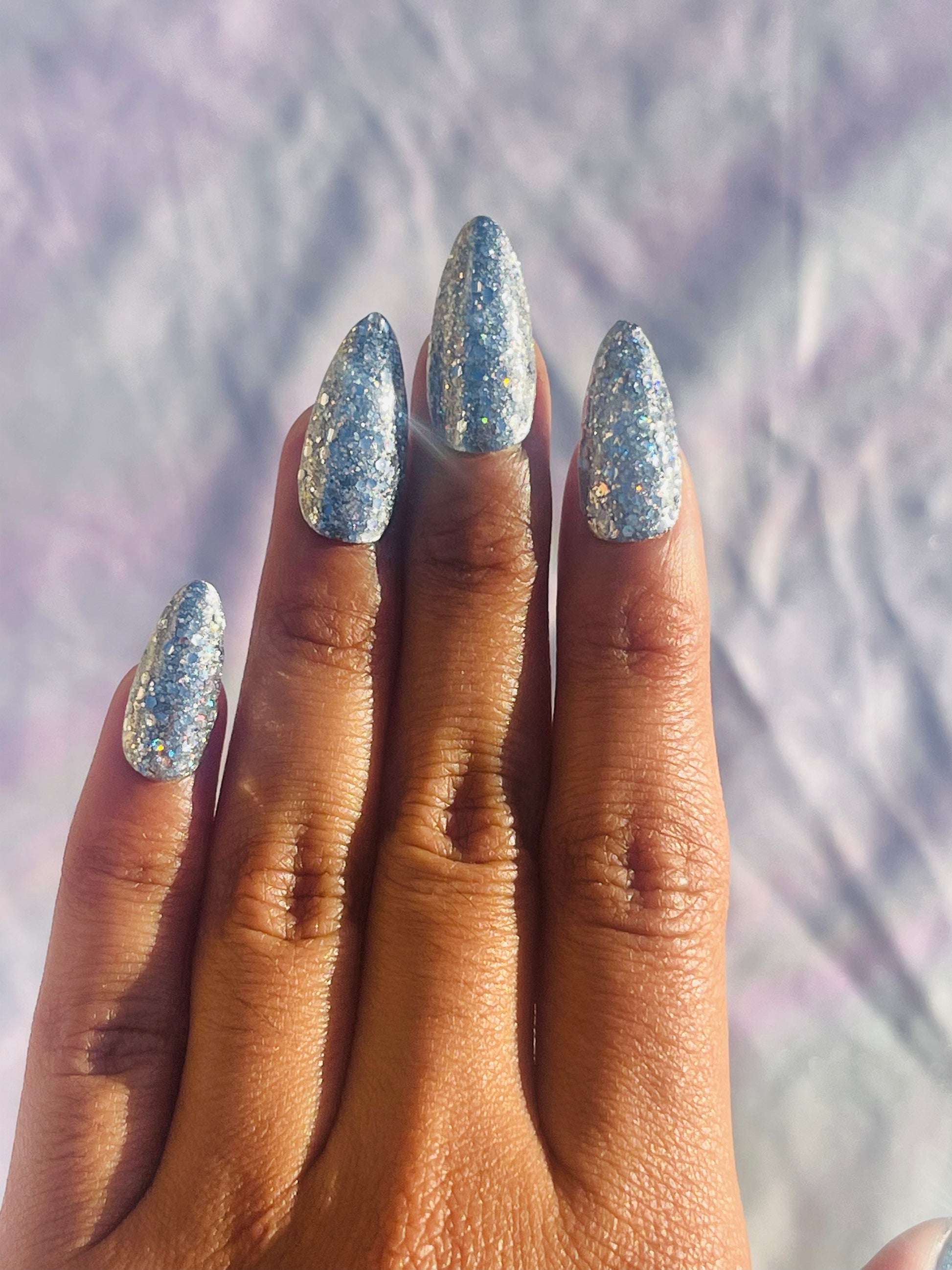 A set of medium-length, almond-shaped nails covered in silver glitter, showcasing a sparkling and elegant appearance.