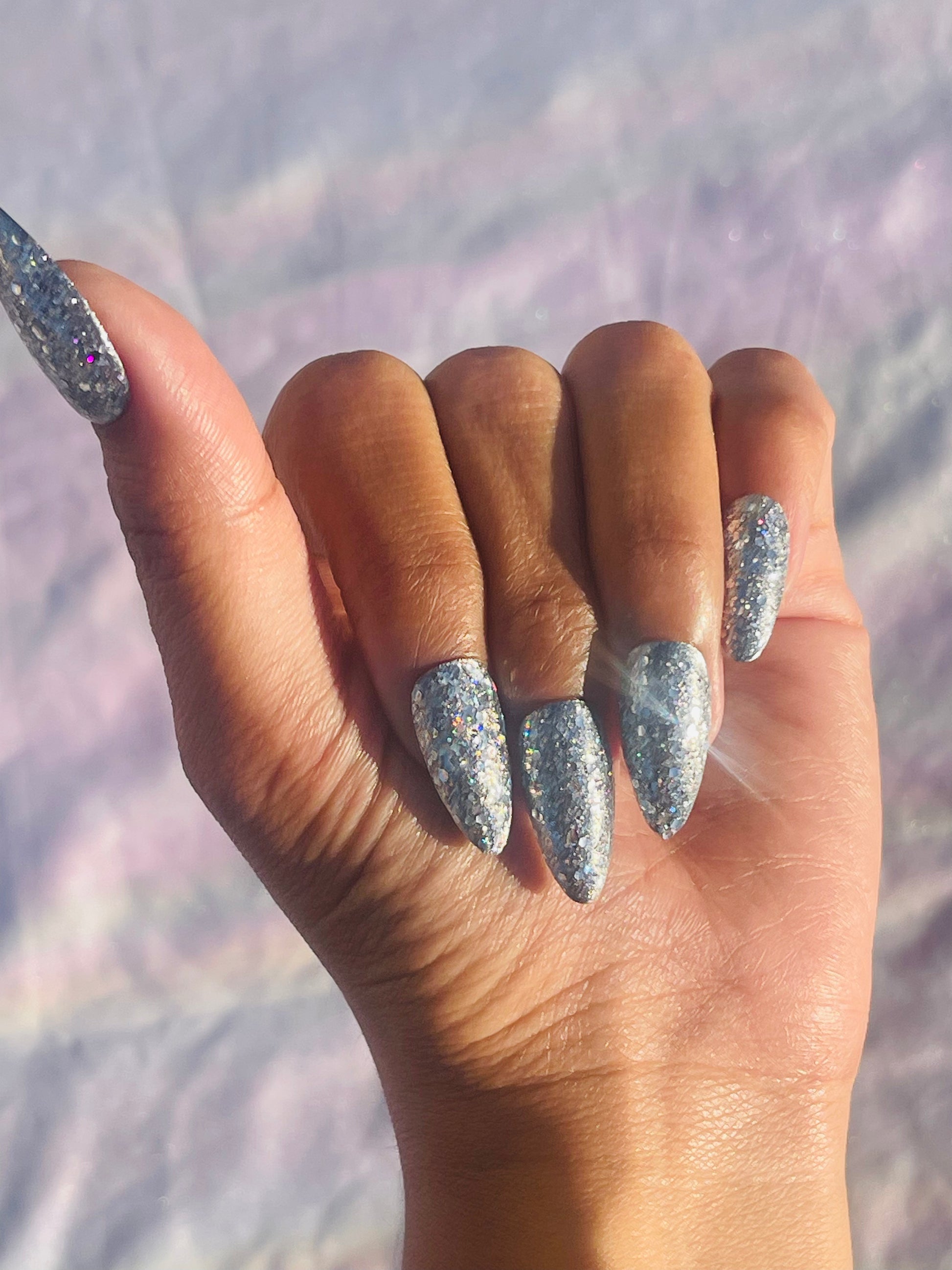 A set of medium-length, almond-shaped nails covered in silver glitter, showcasing a sparkling and elegant appearance.