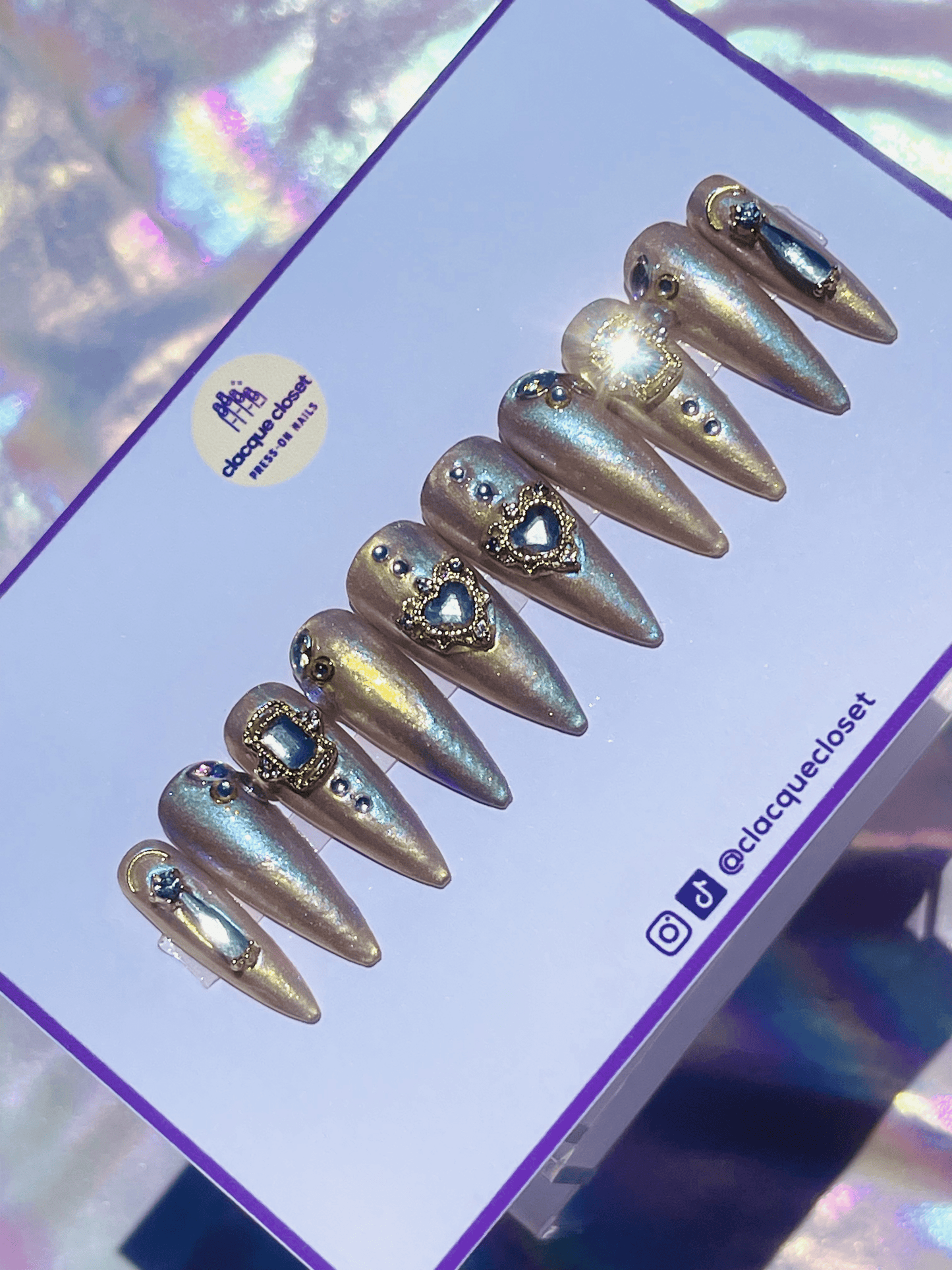 Long stiletto-shaped press-on nails in yellow and blue with a shimmery finish, featuring gold and rhinestone charms for an elegant and eye-catching look.
