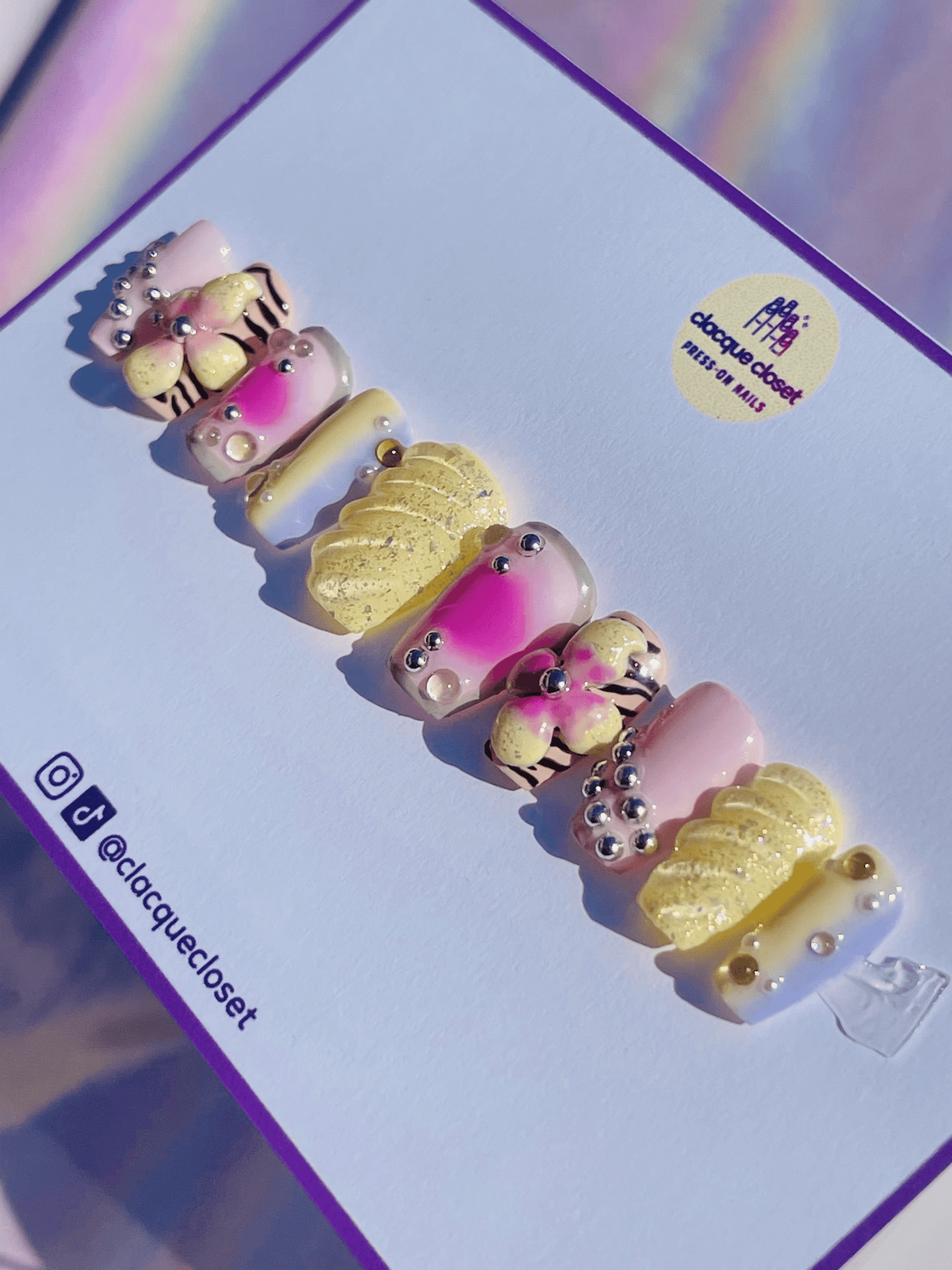 Press-on nails in pastel colors adorned with 3D flowers and charms, creating a delicate and whimsical design.