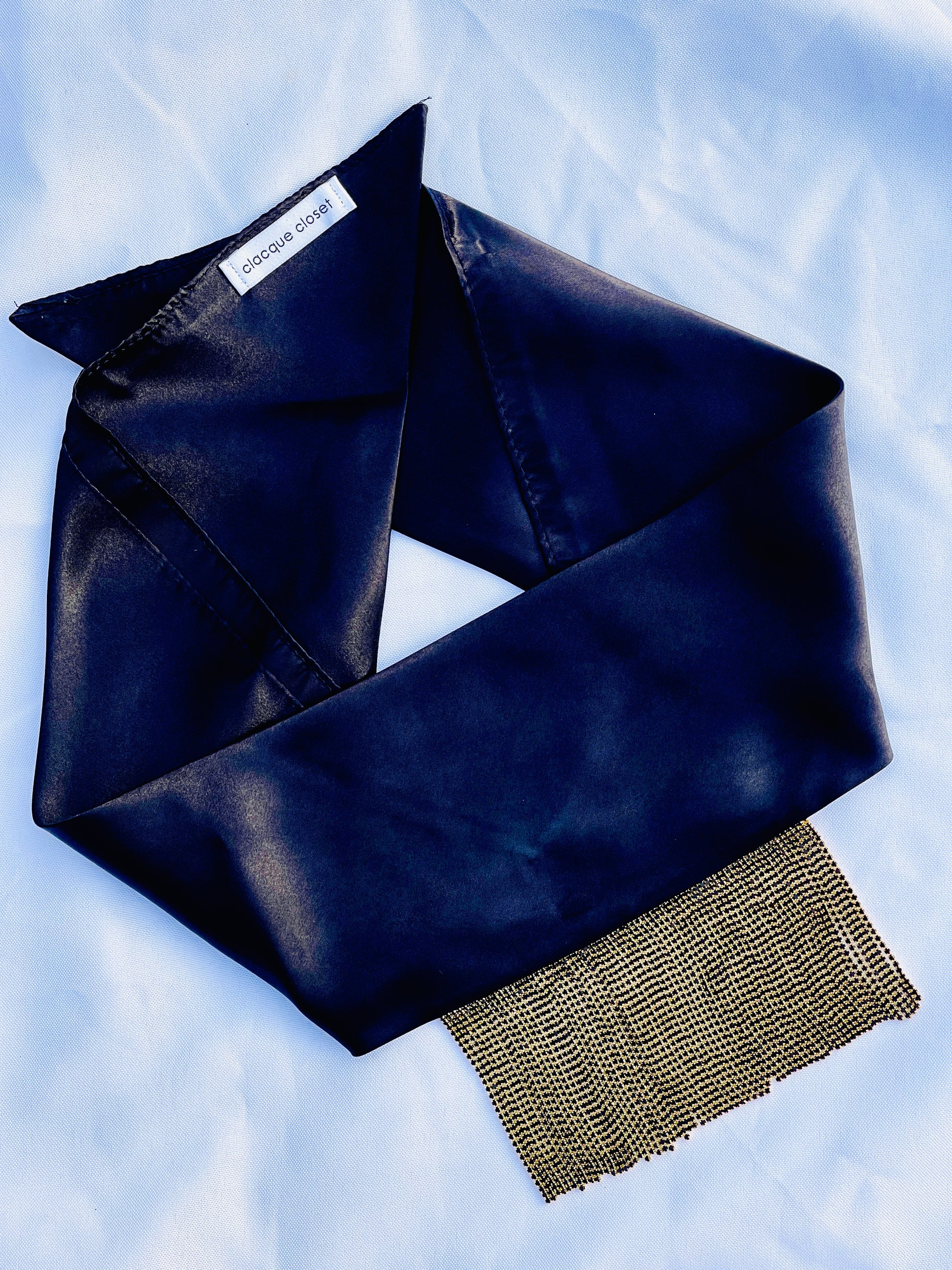 Minerva black satin bandana bang with gold fringe laid flat.