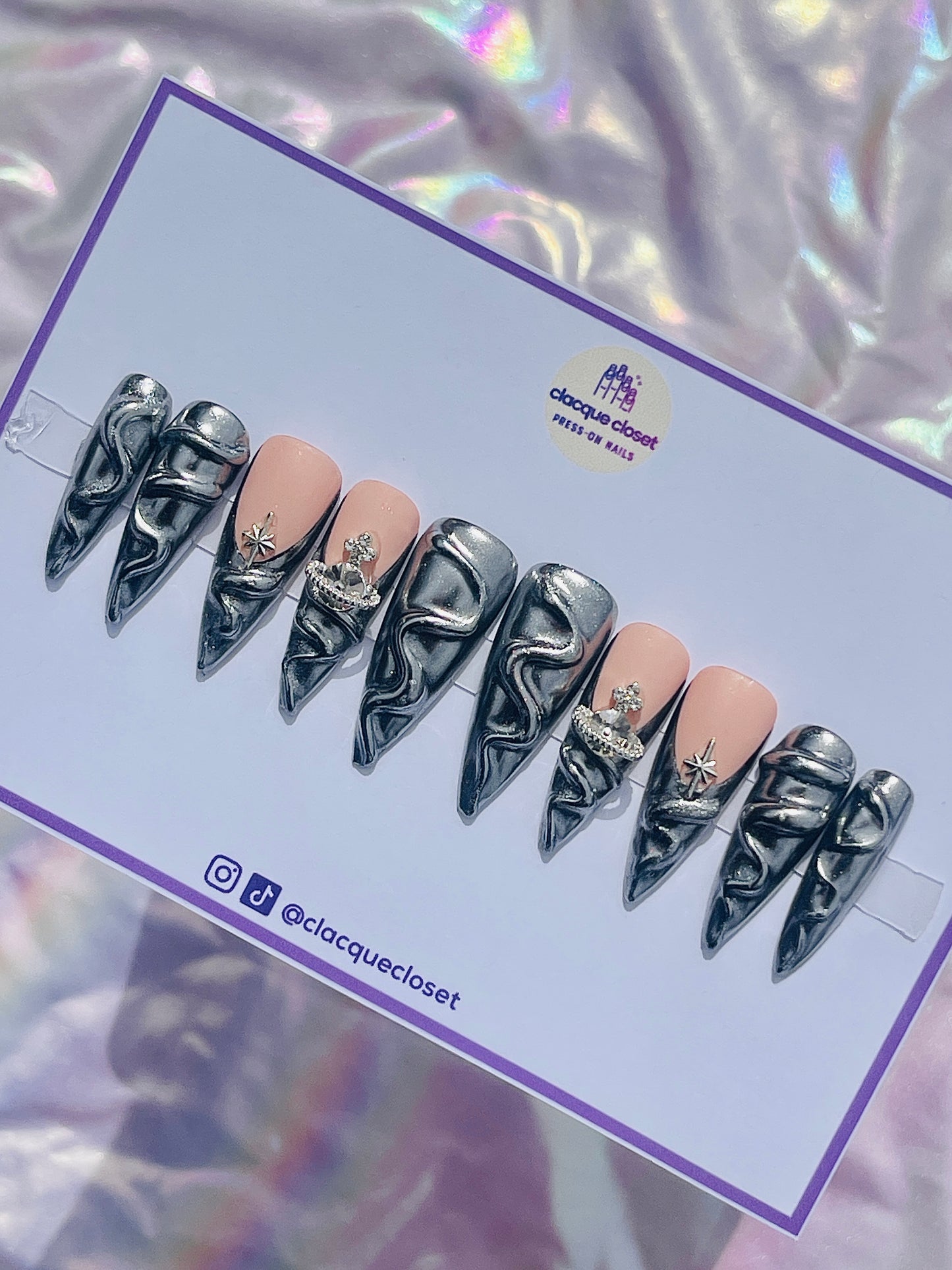 Long stiletto nails coated in a reflective silver chrome finish, adorned with three-dimensional accents for a striking and futuristic look.