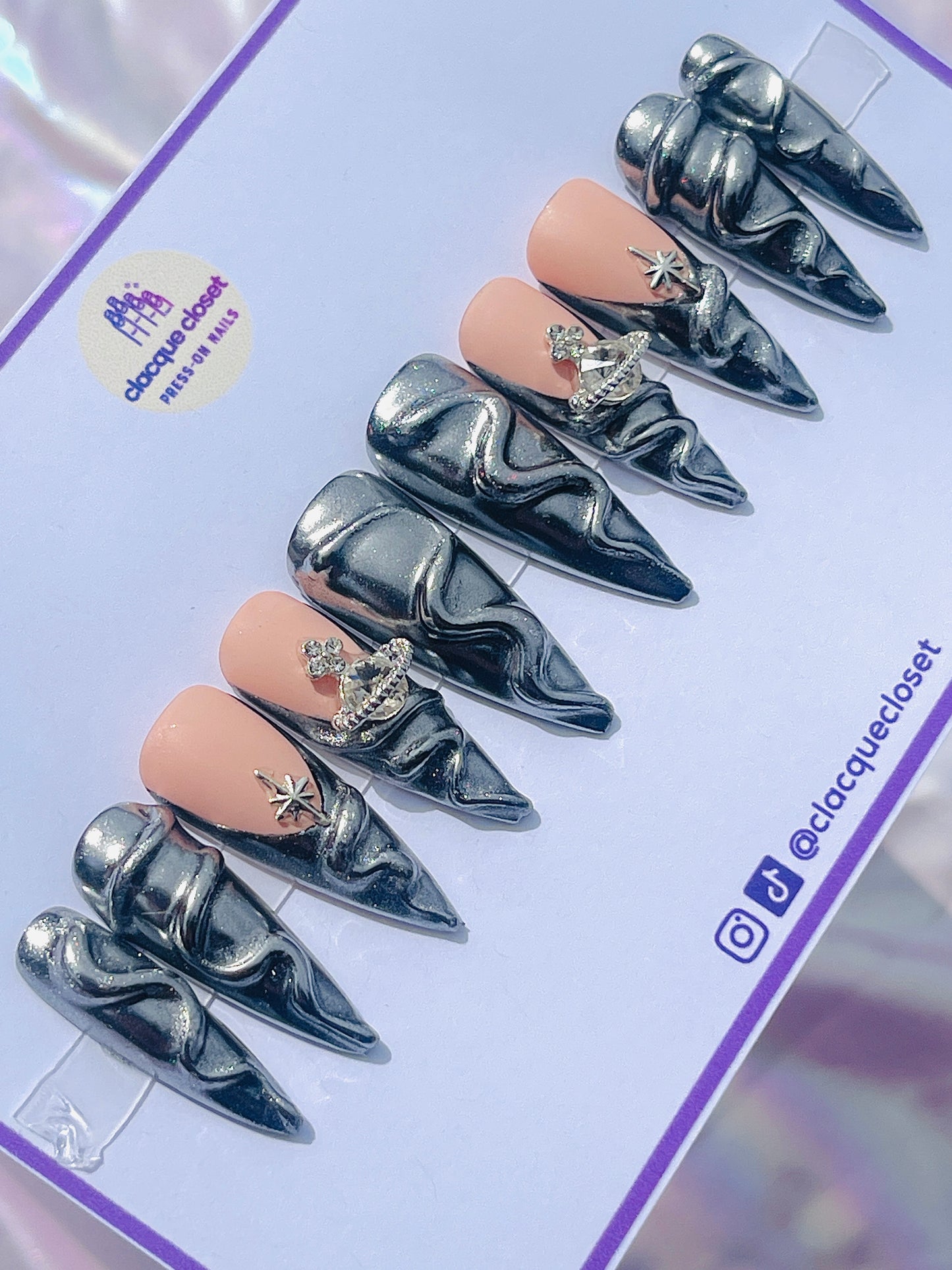 Long stiletto nails coated in a reflective silver chrome finish, adorned with three-dimensional accents for a striking and futuristic look.