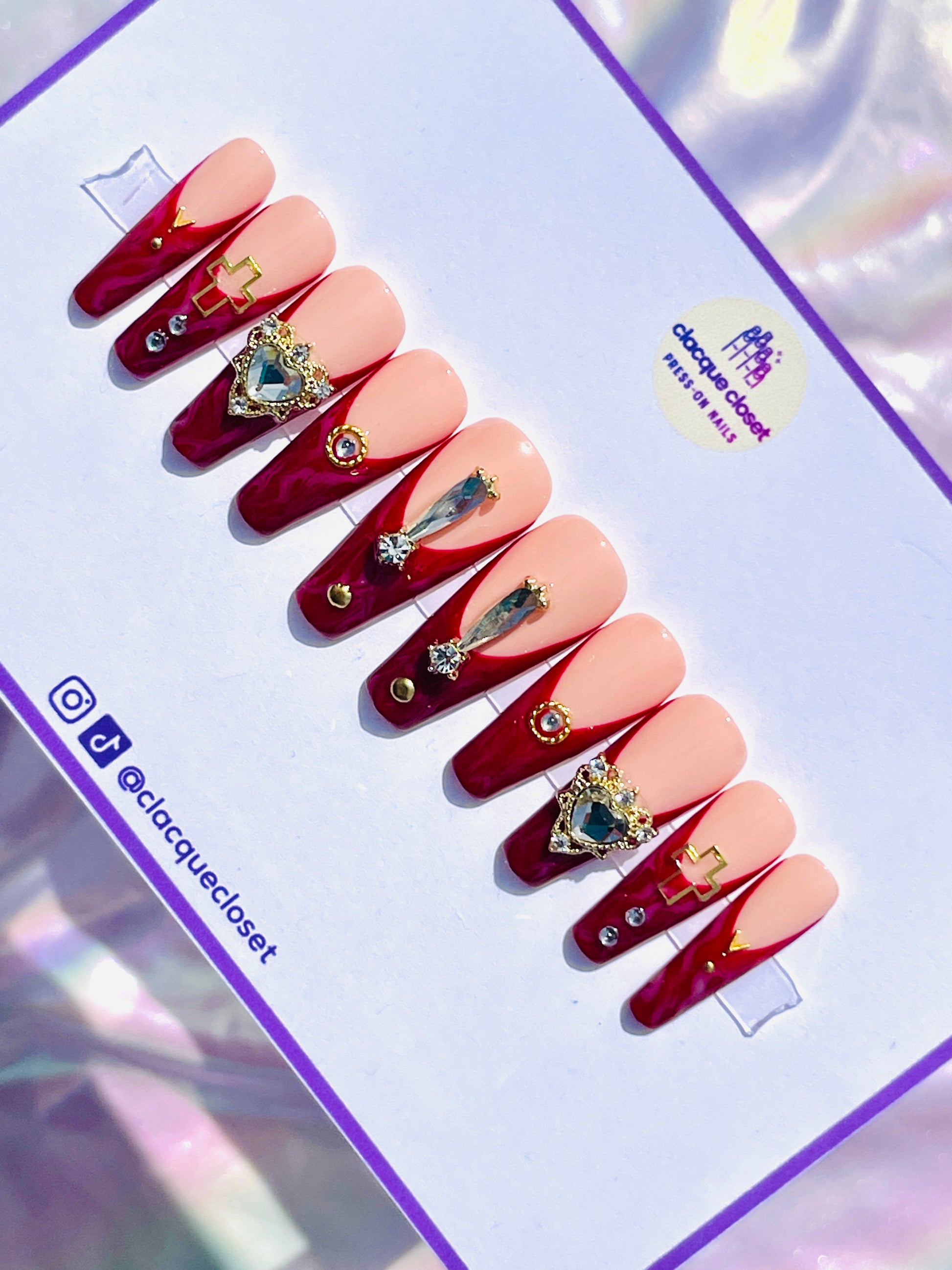 Long coffin-shaped nails with a red marble effect and classic French tips, enhanced with bold rhinestone embellishments and gold accents for a dramatic and luxurious appearance.