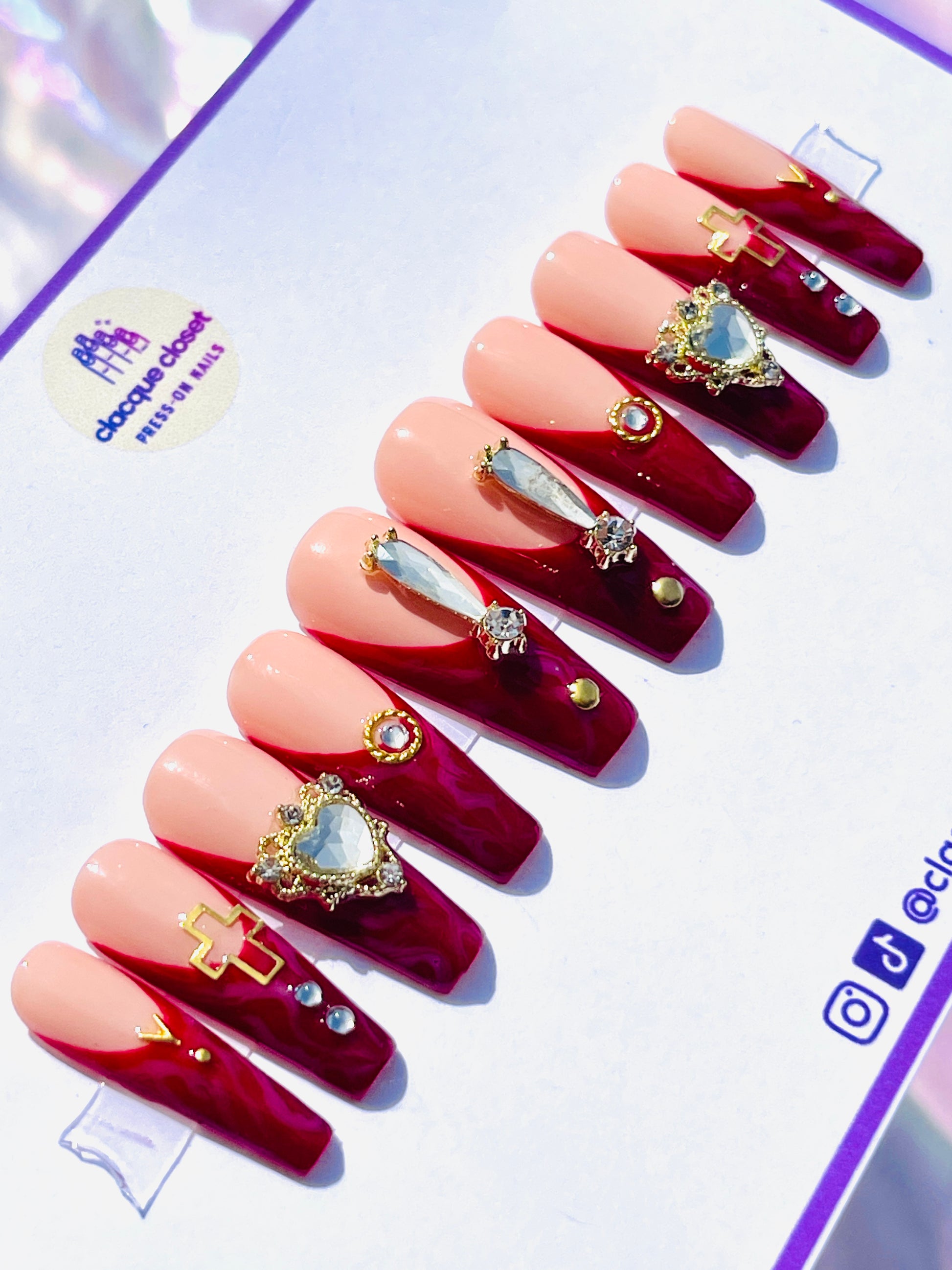 Long coffin-shaped nails with a red marble effect and classic French tips, enhanced with bold rhinestone embellishments and gold accents for a dramatic and luxurious appearance.