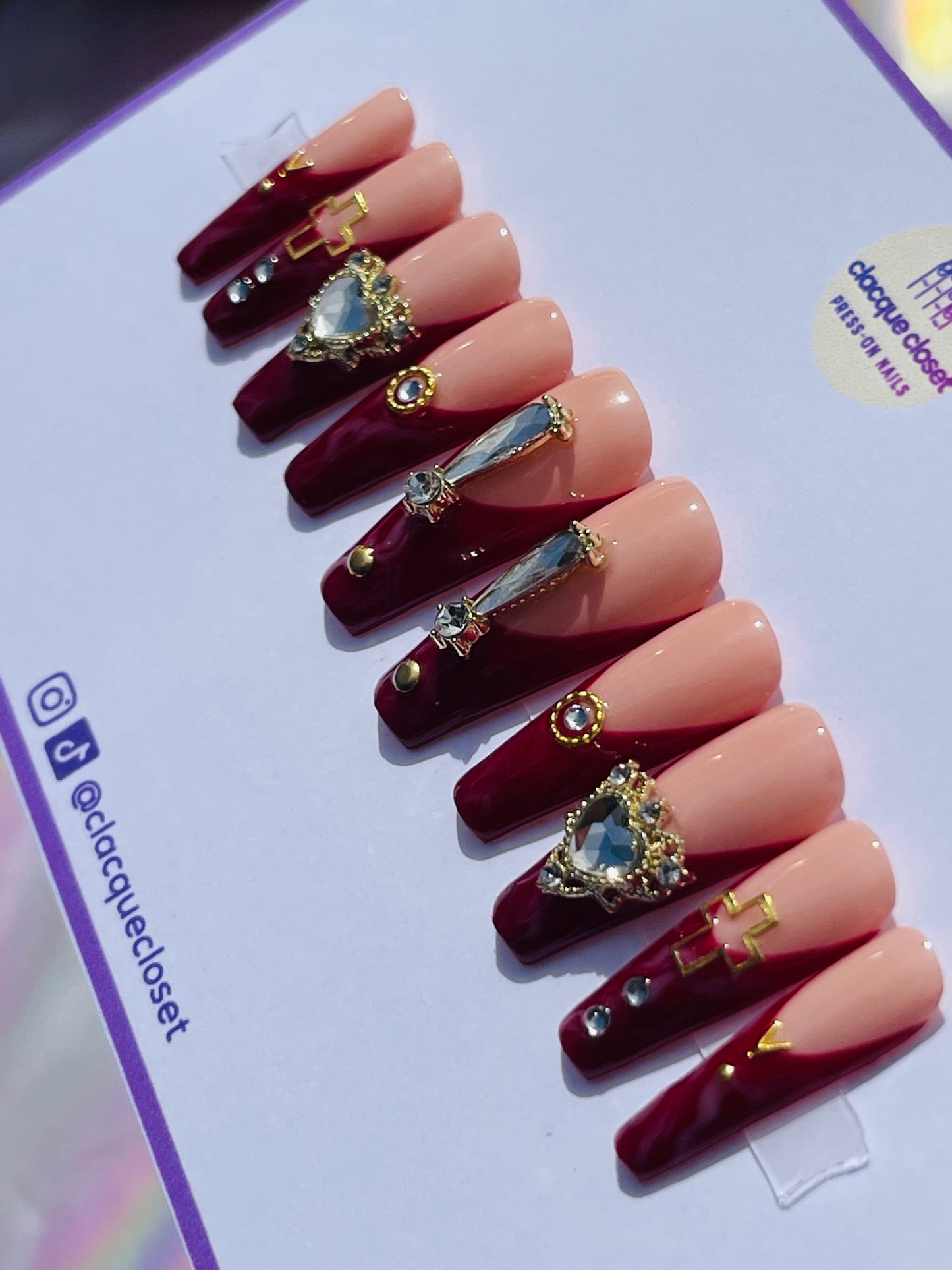 Long coffin-shaped nails with a red marble effect and classic French tips, enhanced with bold rhinestone embellishments and gold accents for a dramatic and luxurious appearance.