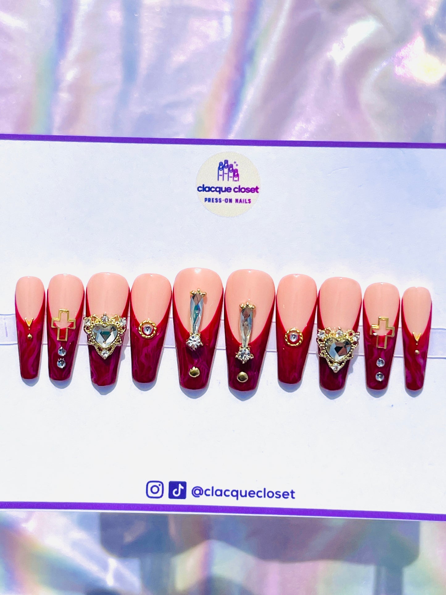 Long coffin-shaped nails with a red marble effect and classic French tips, enhanced with bold rhinestone embellishments and gold accents for a dramatic and luxurious appearance.